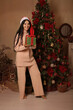 © Тамара Киреева - a beautiful brunette girl with long hair in a Santa Claus hat in pink pajamas is standing at the Christmas tree in the hands of a gift box