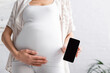 © LIGHTFIELD STUDIOS - cropped view of pregnant young woman holding smartphone with blank screen.
