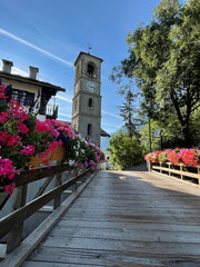 Wall Mural - Wooden bridge approaching a church tower in the Italian alpine village of Sauze de Cesana