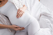 © LIGHTFIELD STUDIOS - top view of pregnant woman touching belly while lying in bed.