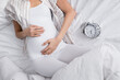 © LIGHTFIELD STUDIOS - cropped view of pregnant woman near alarm clock on bed.