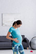 © LIGHTFIELD STUDIOS - cheerful pregnant sportswoman touching belly in living room.