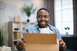 Excited male influencer opening box with ordered goods while staying at home. African american man creating new content for his social networks.