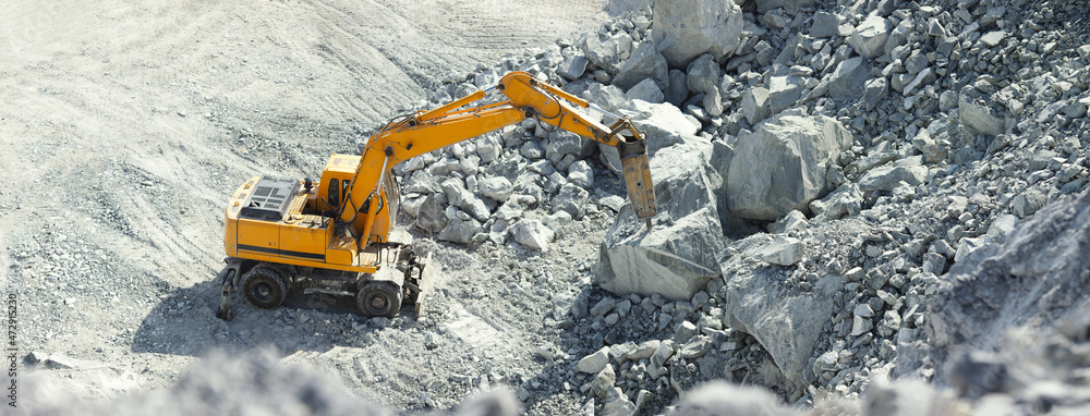 Hydraulic hammer works in a quarry against the background of huge gray stones, panorama.