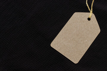 Price tag or blank cardboard label with thread isolated on the black cloth. Great for clothing or fashion mockups.