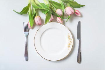 Wall Mural - Spring holiday place setting; Top view of white plate, fork and knife and bouquet of pink tulips above