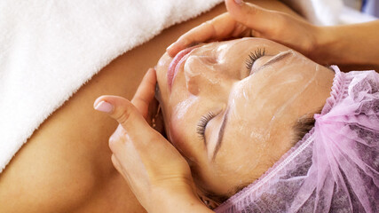 Wall Mural - Woman in a spa salon on cosmetic procedures for facial care. Cosmetologist applies  a cosmetic cream  on female face.  Beauty treatment.