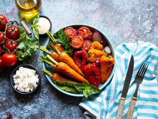 Wall Mural - baked grill baby carrots, tomato, bell pepper in a plate, basil and spices vegan dish close up, white sauce