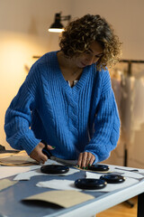 Wall Mural - Female tailor cutting clothing samples with scissors of cardboard pattern drafts paper in garment factory design studio. Sewer create layout for clothes models. Fashion designer at work in atelier