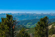 Bergige Landschaft in Österreich.  Blick von einem hochgelegenen Punkt auf  eine Gebirgskette im Vordergrund befinden sich Nadelbäume.  Sonniger Herbsttag
