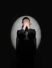man in suit with closed covers eyes with  hands. Elegant style black and white symmetrical composition of strong sad negative emotions. Hide inside. infantile behavior. circle spotlight