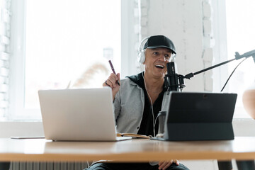 Portrait of a fashionable radio host pro age man working in a recording studio. A blogger communicates with people through a microphone.