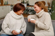 Happy loving family mother and grown up daughter sitting in kitchen decorated on Christmas enjoying hot tea and talking to each other. Christmas and New Year concept
