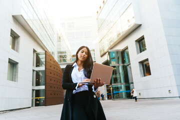 elegant hispanic businesswoman consulting financial operations on her laptop on the street.