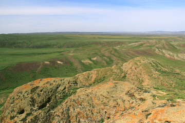 Wall Mural - Green valley of the Malaysary ridge, in the foreground there are red rocks, distant view of the valley plateau, sky with clouds, summer, sunny