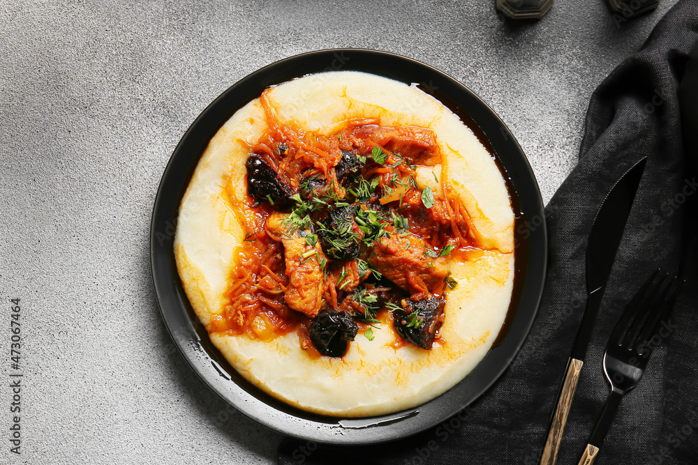 Plate with delicious mashed potatoes, beef stew with prunes and cutlery on grey table