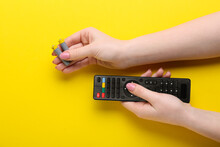 Woman Holding TV Remote Controller And Batteries On Yellow Background