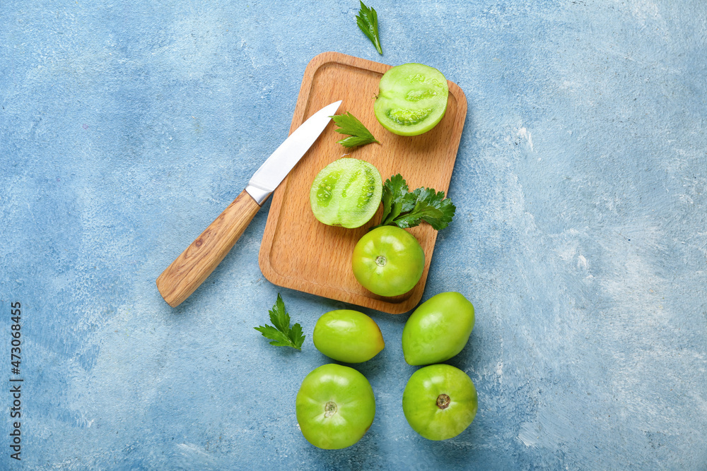 Wooden board with green tomatoes and knife on color background
