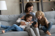 © fizkes - Happy mom and cheerful excited two kids making video call on smartphone, taking funny selfie photo, watching online media on mobile phone, holding cellphone, relaxing on comfortable couch at home