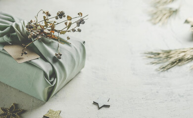 Christmas background with  sustainable gift packaging made with grey fabric and small branch. Plastic free lifestyle. Zero waste concept. Front view.