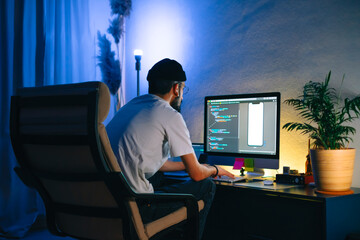 Young man mobile developer writes program code on a computer, programmer work in home office.