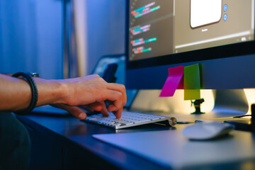 Mobile developer writes program code on a computer, typing on keyboard, programmer work in home office.