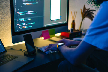 Young man mobile developer writes program code on a computer, programmer work in home office.