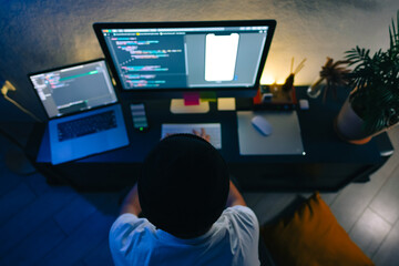 Young man mobile developer writes program code on a computer, programmer work in home office.