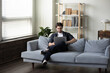 © fizkes - Smiling focused millennial man in casual using laptop computer on comfortable couch in living room. Relaxed freelance worker, employee guy working from home, watching learning business webinar