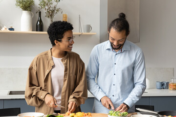 Wall Mural - Happy sincere affectionate young married African American family couple enjoying preparing healthy weekend meal together in modern kitchen, chopping organic vegetables for salad, culinary hobby.