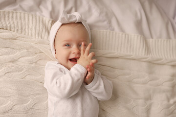 a 6-month-old baby lies in a crib in the nursery with white clothes on her back and laughs, looks at the camera, the morning of the child, the concept of children's goods. high-quality photography