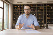© fizkes - Serious confident millennial business professional in glasses looking at camera, holding online video call. Young business man, employee, coach giving webinar screen view head shot portrait