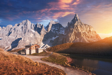 Wall Mural - Incredible landscape with a reflection of purple sky and mountains in a water of small lake in a popular tourist destination - Baita Segantini mountain refuge. Rolle Pass, Dolomites Alps, Italy