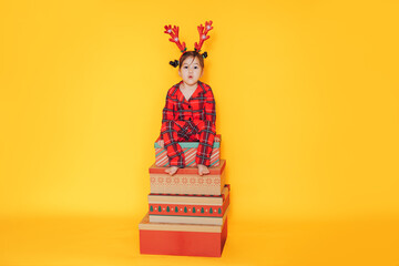 Wall Mural - Girl in red pajamas sitting on gift boxes against yellow background.