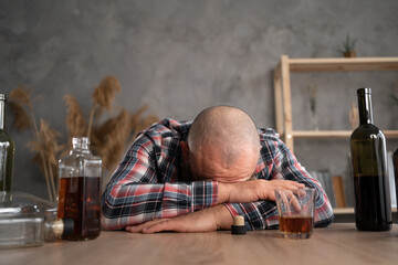 alcoholism, alcohol addiction and people concept - alcoholic man lying or sleeping on the table during the day among empty bottles of alcohol.