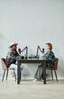 © Seventyfour - Vertical full length portrait of two people speaking to microphones while recording podcast in studio