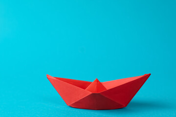 Sticker - Handmade red paper boat on light blue background.  Origami art