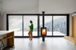 Woman standing with phone near fireplace at modern living room with great view on snowy mountains. Concept of rest in houses or cabins on nature. Solitude in nature and escape from everyday life
