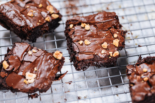 Chocolate brownies with hazelnut crumbs on top, on a tray with cacao powder, chocolate crumbs on a white rustic background. Very fudge brownies