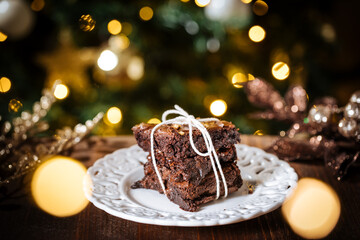 Wall Mural - Chocolate brownies wrapped in group as a present in front of Christmas tree with Christmas lights in festive atmosphere and decoration