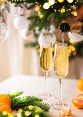 Two glasses of champagne and tangerines on a table against blurred christmas background with christmas lights. New year celebration party