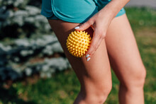Spiky Rubber Massage Ball In Hands Of Young Woman In Shorts For Cellulite Reduction And Weight Loss On Lawn In Garden On Summer Morning. 