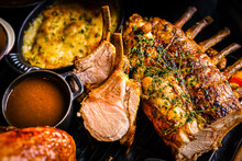 Roasted Rack Of Lamb With Herbs, Grilled Vegetable Side Dish, Gravy Or Jus And Mint Sauce Over Dark Background With Copy Space. Sharing Party Concept. Top View, Flat Lay Shot. Colorful, Modern Setting