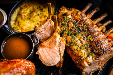 Wall Mural - Roasted Rack of Lamb with herbs, grilled vegetable side dish, gravy or jus and mint sauce over dark background with copy space. Sharing Party Concept. Top view, Flat Lay shot. Colorful, Modern setting