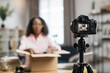 © sofiko14 - Blur background of young african woman unboxing parcel and recording video blog. Focus on modern digital camera. Concept of social networks technology.