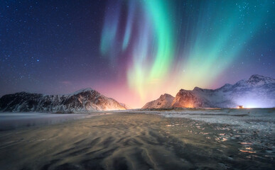Wall Mural - Aurora borealis above the snowy mountain and sandy beach in winter. Northern lights in Lofoten islands, Norway. Starry sky with polar lights. Night landscape with aurora, frozen sea coast, city lights
