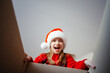 © Анна Молько - cute girl in a red sweater and santa claus hat opens a box with gifts for christmas. sincere joy and happiness. children's open emotions