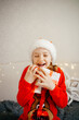 © Анна Молько - cute little girl in red sweater and santa claus hat rejoices with gifts for christmas. sincere joy and happiness. children's open emotions