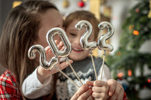 Happy Mom And Son On The Background Of A Christmas Tree Are Holding In Their Hands The Silver Numbers 2022 On Sticks. Concept Of The New Year, Festive Atmosphere, Home Decoration, Congratulation