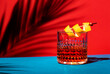 Sazerac, classic alcoholic cocktail with cognac, bourbon, absinthe, bitters, sugar and lemon zest. Dazzling red blue background with hard light and harsh shadows